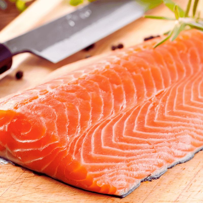 Filete de salmón con piel sobre tabla de madera y un cuchillo de fondo