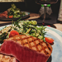 Plato gourmet con porción de atún rojo acompañado de ensalada y una copa de vino