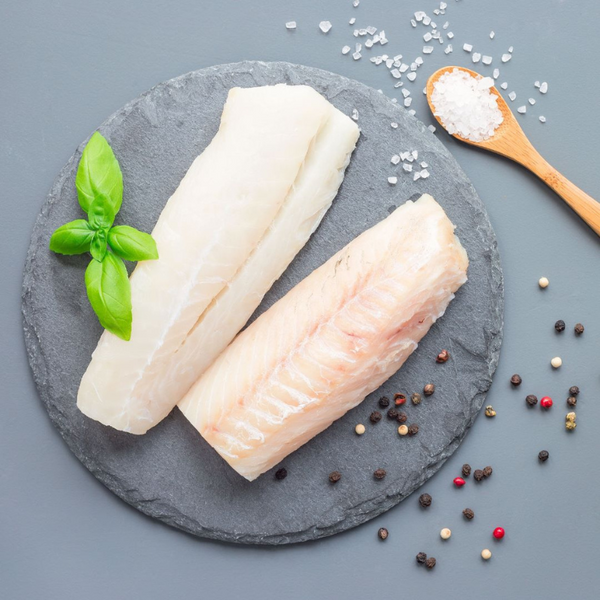 Dos filetes de congrio dorado sobre un plato de piedra con pimienta y albahaca