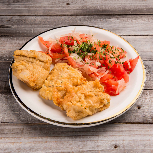 Plato con tres porciones de congrio dorado frito con ensalada chilena sobre una mesa de madera