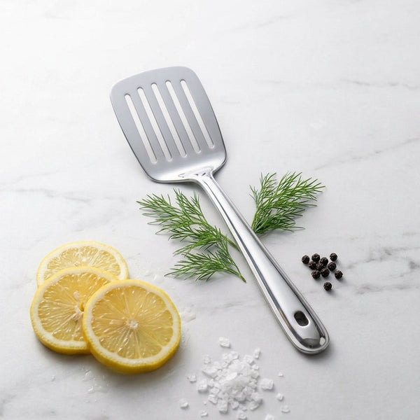 Espatula de acero inoxidable sobre una mesa adornada por rodajas de limon y hierbas