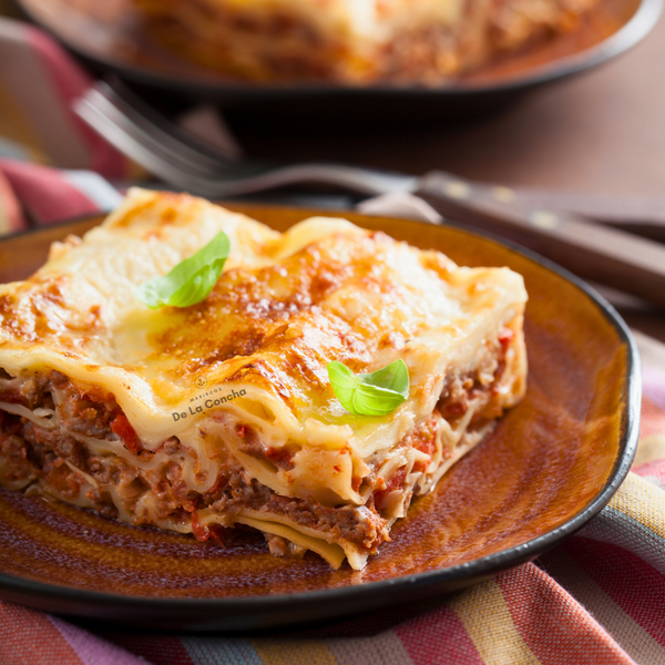 Porción de lasagna bolognesa sobre plato café aderezada con hojas verdes