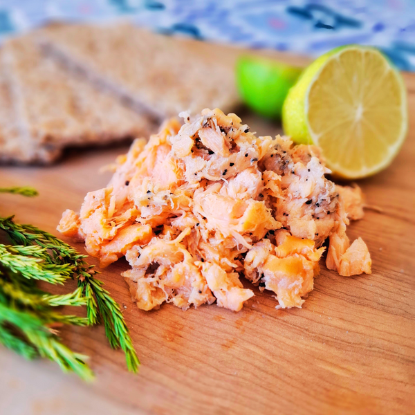 Recorte de Salmon Ahumado en caliente a la pimienta sobre tabla de madera adornado con hojas verdes y limón