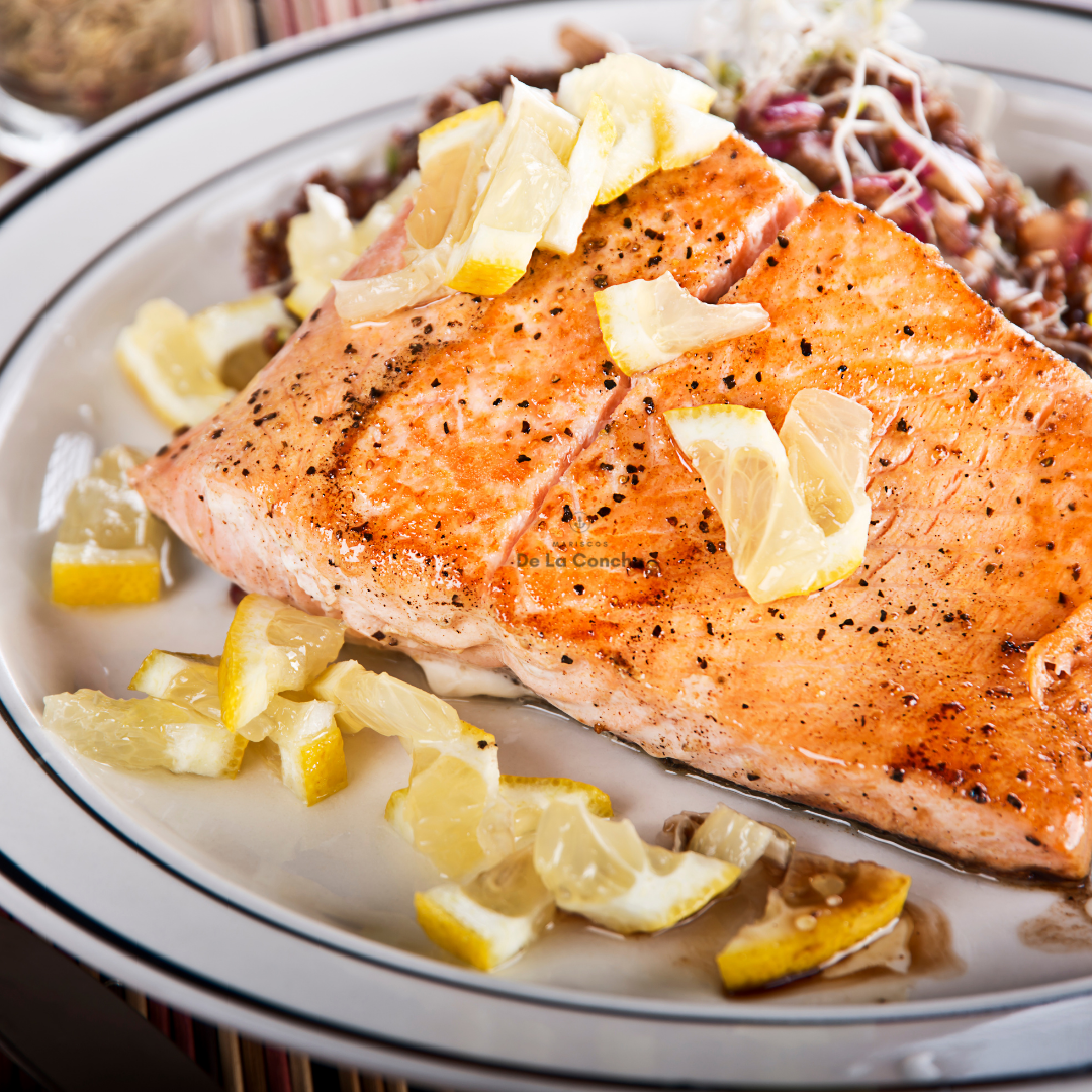 Trozo de salmon cocinado sin piel con pimienta y gajos de limon sobre plato blanco