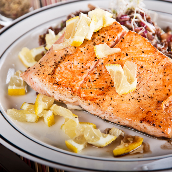 Trozo de salmon cocinado sin piel con pimienta y gajos de limon sobre plato blanco