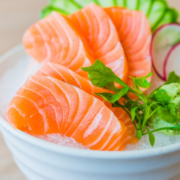 Piezas de Sashimi de salmon con hojas verdes en un plato blanco